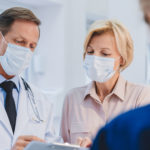 Doctor with patient and female receptionist working in medical protective masks in clinic lobby. Epidemic prevention concept