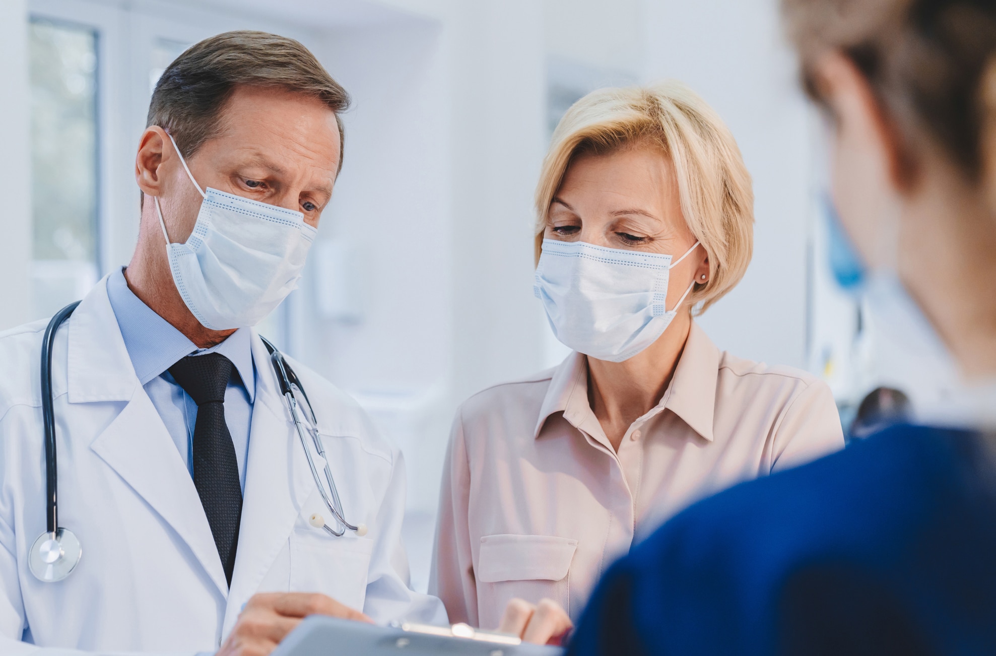 Doctor with patient and female receptionist working in medical protective masks in clinic lobby. Epidemic prevention concept