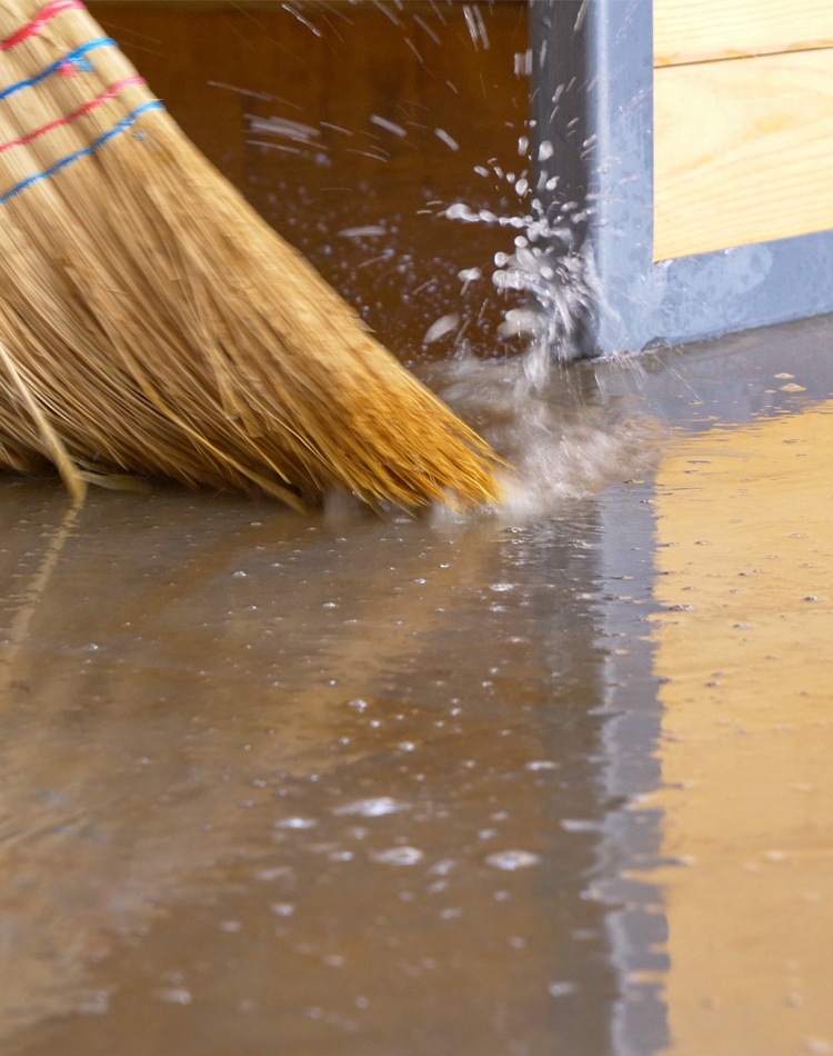 Broom with rough straw bristles sweeps away the dirty water covering the basement floor.