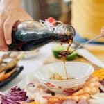 Woman pouring couple of tea spoons of soy sauce into small bowl when making dipping sauce for snack plate