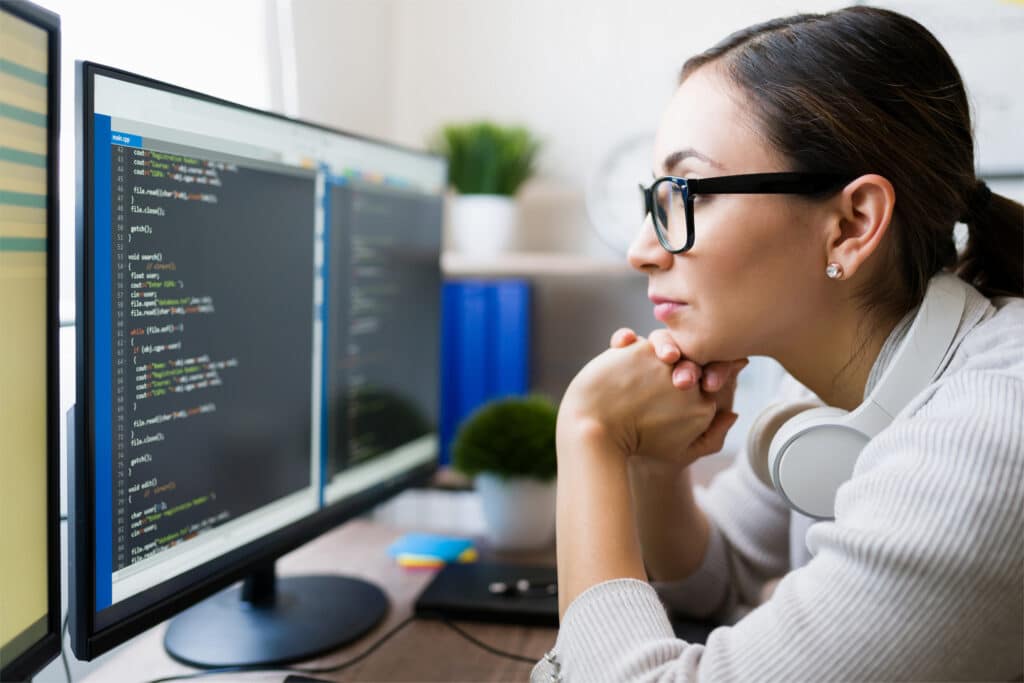 Profile of a hispanic freelancer wearing glasses and reading the coding software on the computer. Focused programmer checking the app code.